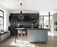 Cuisine ouverte chic avec îlot central au façades mates de couleur vert eucalyptus et un coin repas